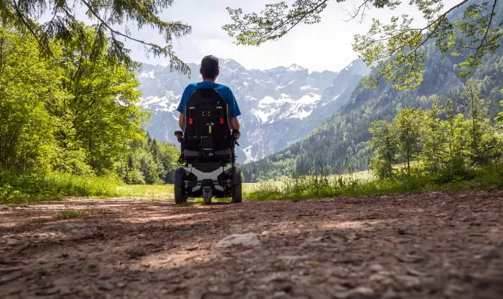 Man on a wheelchair relaxing in nature and looking at mountains on a sunny summer day.