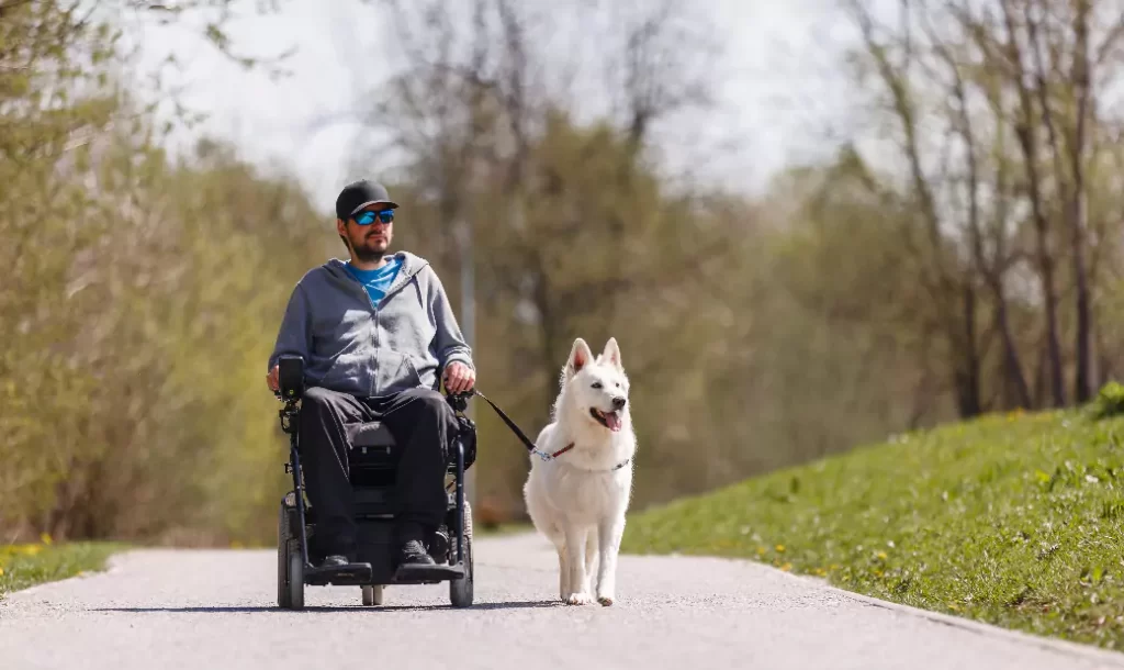 Man with disability outside in park with his service dog using electric wheelchair.