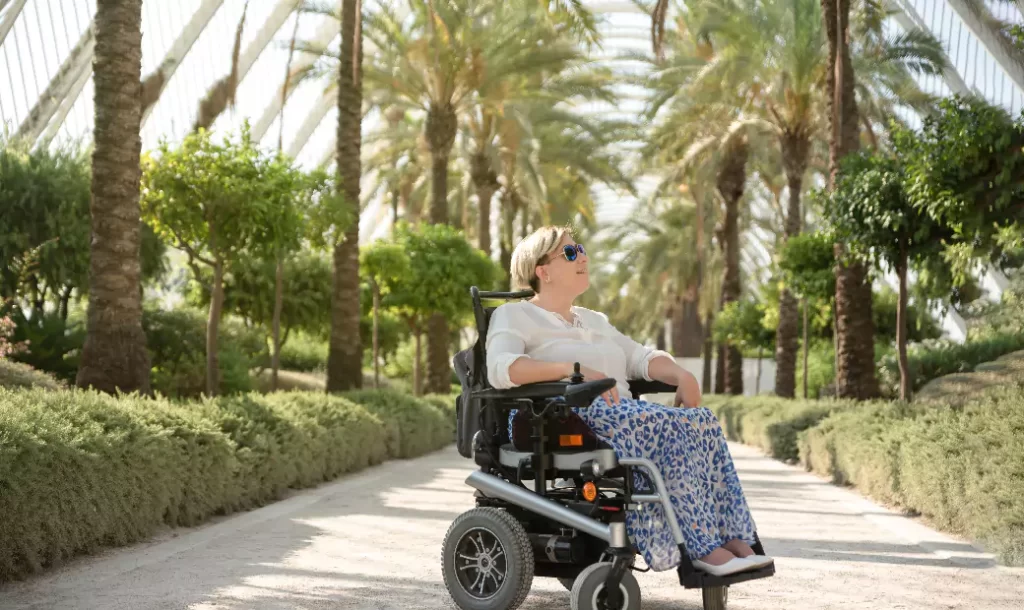a-smiling-woman-sitting-in-the-electric-wheelchair-with-disability-enjoys-a-sunny-day-in-the-garden-of-the-city-park