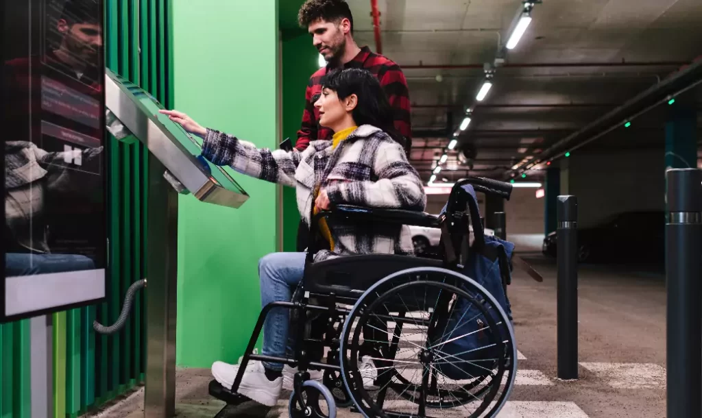 a-woman-in-a-wheelchair-is-assisted-by-a-man-to-make-a-payment-at-an-accessible-parking-meter