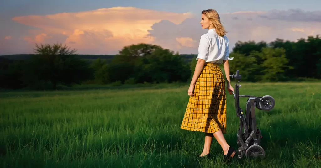 The woman was walking on the grass with a folded wheelchair in her hands.