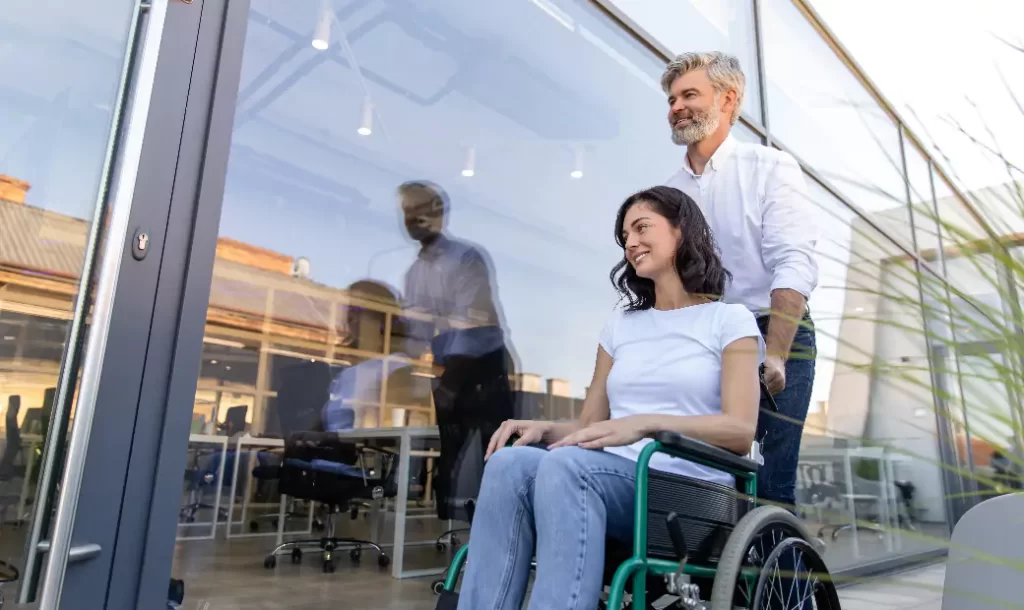 The man is pushing his wife who is sitting in a wheelchair.