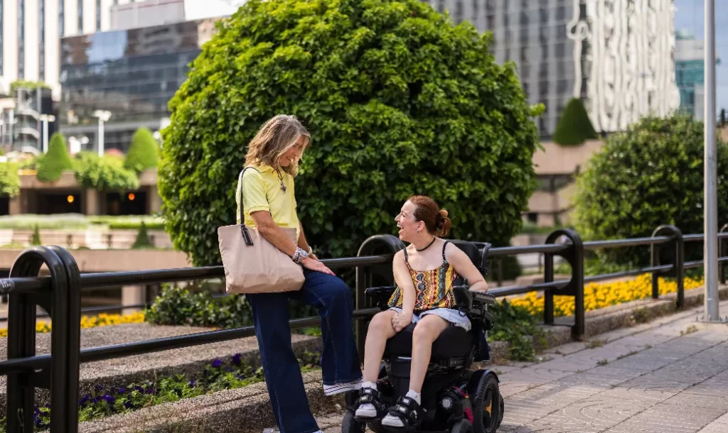 Two women, one sitting in an electric wheelchair, were chatting on a vibrant city street.