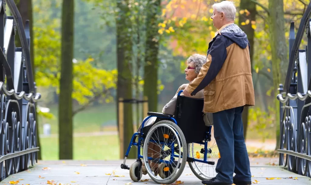 old-couple-in-the-park-woman-sitting-on-a-wheelchair-and-man-standing-behind